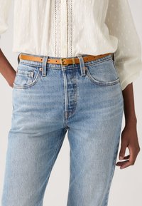 Ανοιχτό μπλε τζιν παντελόνι με άνετη εφαρμογή και ψηλό καβάλο, σε συνδυασμό με μια καφέ δερμάτινη ζώνη. Το ύφασμα έχει απαλή υφή και διακριτική ξεθώριαση.