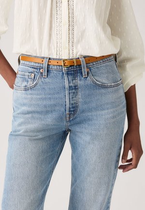 Vaqueros de mezclilla azul claro con un corte relajado y cintura alta, combinados con un cinturón de cuero marrón claro. La tela tiene una textura suave y un desvanecimiento sutil.