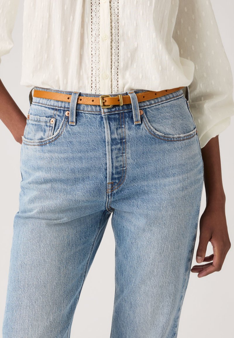 Ανοιχτό μπλε τζιν παντελόνι με άνετη εφαρμογή και ψηλό καβάλο, σε συνδυασμό με μια καφέ δερμάτινη ζώνη. Το ύφασμα έχει απαλή υφή και διακριτική ξεθώριαση.