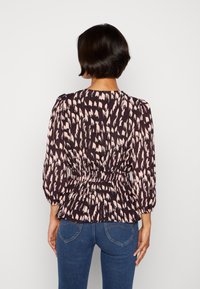 Dunkel gemusterte Bluse mit einem pinken abstrakten Design, elastischem Bund und voluminösen Ärmeln, kombiniert mit blauen Jeans.