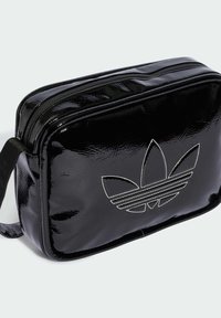 Borsa sintetica nera e lucida con chiusura a zip, caratterizzata da un logo Adidas in rilievo e cuciture bianche. Forma rettangolare con base piatta.