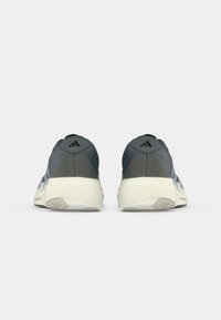 Zapatillas grises con una parte superior de tela texturizada, que presentan una media suela blanca y tres franjas azules a lo largo del costado. Logo en el talón.