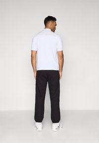 Men's outfit: short-sleeve white top, black textured joggers, elastic cuffs, and white sneakers. Simple, sporty design with a neutral color palette.
