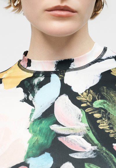 Κοντινή λήψη ενός ατόμου που φοράει τοπ με floral σχέδιο και ψηλό λαιμό με αφηρημένα παστέλ και πράσινα πινέλα, εμφανίζοντας μόνο τα χείλη και το λαιμό.