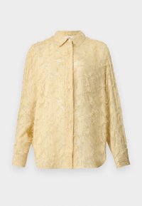 Blusa gialla chiara con maniche lunghe, tessuto testurizzato con dettagli sfrangiati, chiusura a bottoni e colletto definito. Presenta una vestibilità rilassata.