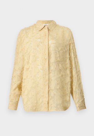 Light yellow blouse with long sleeves, textured fabric featuring frayed detailing, button closure, and defined collar. Features a relaxed fit.