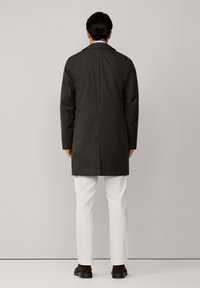 Oliivinvihreä pitkä takki suoralinjaisella leikkauksella, yhdistettynä valkoisiin housuihin ja ruskeisiin kenkiin. Sisältää lovetun kauluksen ja sileän tekstuurin.