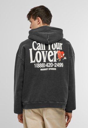 Dunkelgrauer Hoodie mit einem großen Graphic auf dem Rücken, das weißen Text "Ruf deinen Liebhaber an" und eine Cartoon-Herzfigur zeigt.