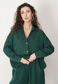 Zielona koszula zapinana na guziki wykonana z miękkiej tkaniny, z dwoma kieszeniami na piersiach, długimi rękawami oraz luźnym, oversize'owym krojem.