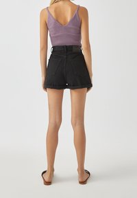 Top sin mangas de canalé morado con un profundo escote en la espalda, combinado con shorts de mezclilla negra de cintura alta. Los shorts tienen dobladillos enrollados y bolsillos traseros.