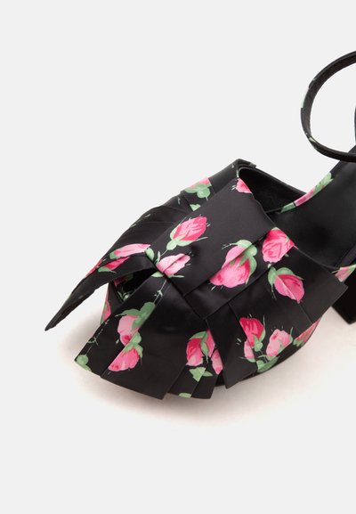Chaussure à talons noire avec motif floral de rose rose et détail superposé en tissu à l'avant, montrant la bride de cheville.