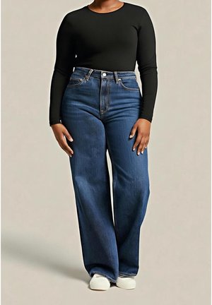 Personne portant un jean bleu taille haute à jambes larges, un haut noir ajusté à manches longues, et des chaussures blanches sans lacets, debout devant un fond uni.