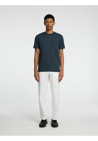 Marine gestreept t-shirt met korte mouwen en een ronde hals, gecombineerd met witte broek. Model draagt zwarte schoenen en staat met de handen langs het lichaam.