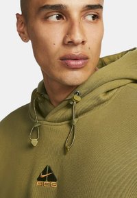 Olijfgroene hoodie met trekkoordsluiting, textuurstof, logo op de borst en verstelbare toggles. Beschikt over een modern, atletisch ontwerp.
