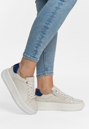 White leather sneakers with blue heel accents and side zipper, worn with light blue skinny jeans on crossed legs.