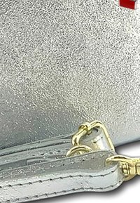 Zilveren metallic clutch met een gestructureerd oppervlak, voorzien van een gouden schouderriem en een kleine rode accent. Afmetingen en merk zijn niet zichtbaar.