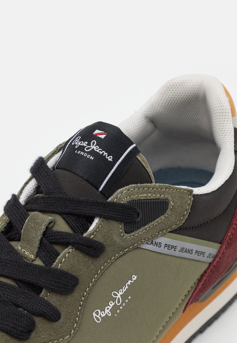 Gros plan d'une basket Pepe Jeans avec des lacets noirs, des panneaux vert olive et bordeaux, une doublure intérieure blanche, et un logo de marque sur la languette et le côté.