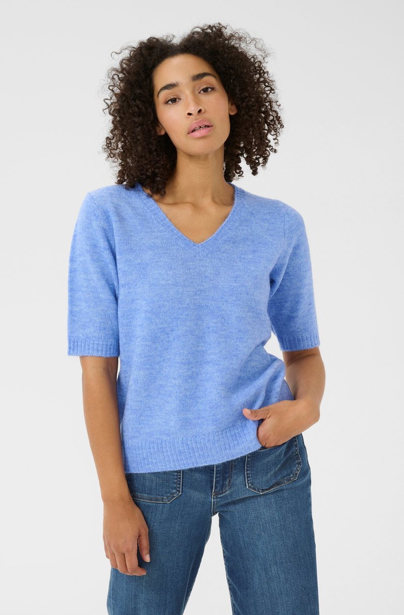 Lichtblauwe korte mouwen trui met V-hals. Zachte textuur en ribbelzoombeslag. Gecombineerd met donkere denim jeans. Neutrale achtergrond.