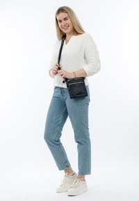 Schwarze Leder-Umhängetasche mit silberner Hardware, ausgestattet mit einer strukturierten Oberfläche und Reißverschluss-Details, kombiniert mit hellblauen Jeans und einem weißen strukturierten Oberteil.