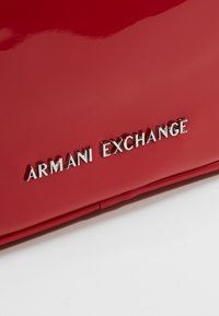 Czerwona torebka z lakierowanej skóry z gładką teksturą i błyszczącym wykończeniem, z logo "ARMANI EXCHANGE" w metalicznych literach.