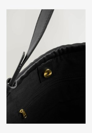 Bolso tote negro con un exterior de cuero suave, parte superior redonda, cierre metálico en dorado y cierre a presión. El interior no está forrado.