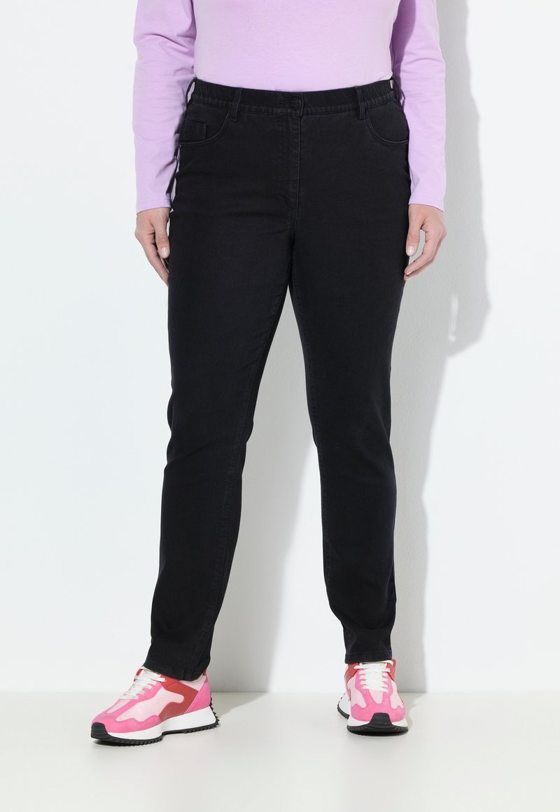 Vaqueros negros de corte slim y cinturilla elástica, complementados con bolsillos frontales. Combinados con zapatillas deportivas en tonos rosa vibrante y blanco.