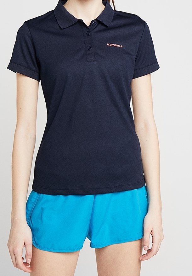 Mörkblå pikétröja i bomullsblandning, med en treknapplösning och en liten röd logotyp. Kombinerad med blå träningsshorts.