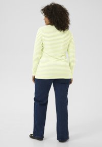 Haut à manches longues, rayé vert lime et blanc, avec un col arrondi, associé à un jean bleu foncé. Le tissu est lisse ; coupe décontractée.