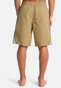 Μπεζ μαγιό με ελαστική μέση, πλευρικές επιφάνειες με καρό σχέδιο και λείο ύφασμα. Το μήκος φτάνει μέχρι το μέσο του μηρού.