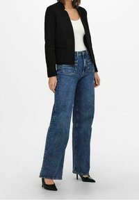 Svart skräddarsydd jacka med en figurnära design, matchad med högmidjade blå vida jeans och svarta spetsskor. Vit linne under.