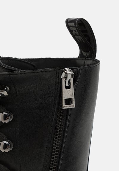 Black leather ankle boot featuring a shiny silver zipper, round laces with metallic eyelets, and a fabric pull tab for easy access.