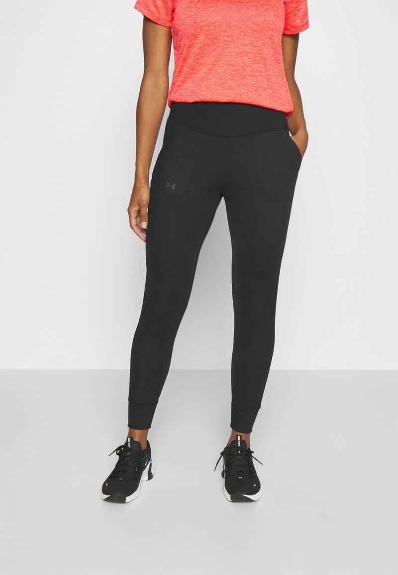 Personne portant un pantalon de jogging noir ajusté avec poches avant et des chaussures de sport noires, associé à un t-shirt corail à manches courtes.