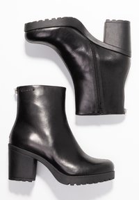 Stivali alla caviglia in pelle nera con tacco a blocco spesso, zip laterale e suola in gomma testurizzata per una presa migliore. Finitura liscia con cuciture minime.