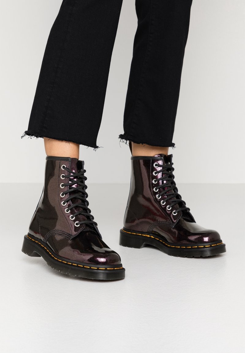 Botas de tobillo de cordones en charol burdeos brillante con cordones negros, que presentan una suela cosida en amarillo y una suela de diseño rugoso.