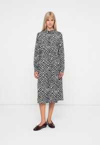 Μαύρο και άσπρο φόρεμα με τύπωμα ζέβρας, μακρυμάνικο, με γιακά, ζώνη στη μέση και κουμπιά μπροστά; Το μοντέλο φορά μπορντό φλατ παπούτσια.