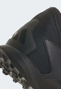 Svart atletisk sko med en texturerad tygöverdel, syntetiska detaljer och en gummiyttersula med multidirektionella greppklackar.