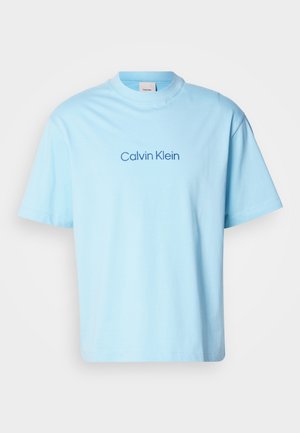 Helles blaues Baumwoll-T-Shirt mit Rundhalsausschnitt und kurzen Ärmeln, das ein zentrales Drucklogo "Calvin Klein" in dunklerem Blau zeigt.