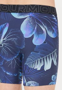 Șorturi de baie de culoare bleumarin cu un model floral tropical în nuanțe de albastru și verde. Prezintă un material texturat și un tiv negru cu marcă.