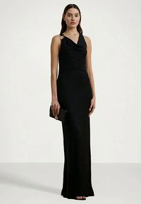 Juoda, bešvinė vakarinė suknelė su raukšlėta iškirpte, prilipęs dizainas ir subtilios drapiruotės. Atitinkanti juoda rankinė su auksiniu akcentu.