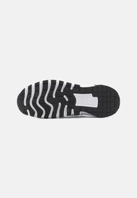 Black rubber sneaker sole with a wavy tread pattern, featuring white accents and grooves for traction and flexibility.