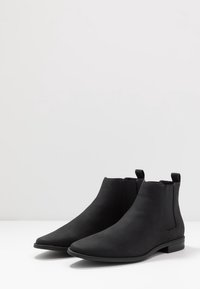 Botines negros de material suave, con un diseño elegante que incluye punteras afiladas, paneles laterales elásticos y un pequeño tacón.