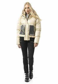 Gesteppte Daunenjacke mit schwarzen Taschen, Reißverschlüssen und Textdetails, kombiniert mit schwarzen, eng anliegenden Hosen und schwarzen Stiefeletten mit Schnallen.