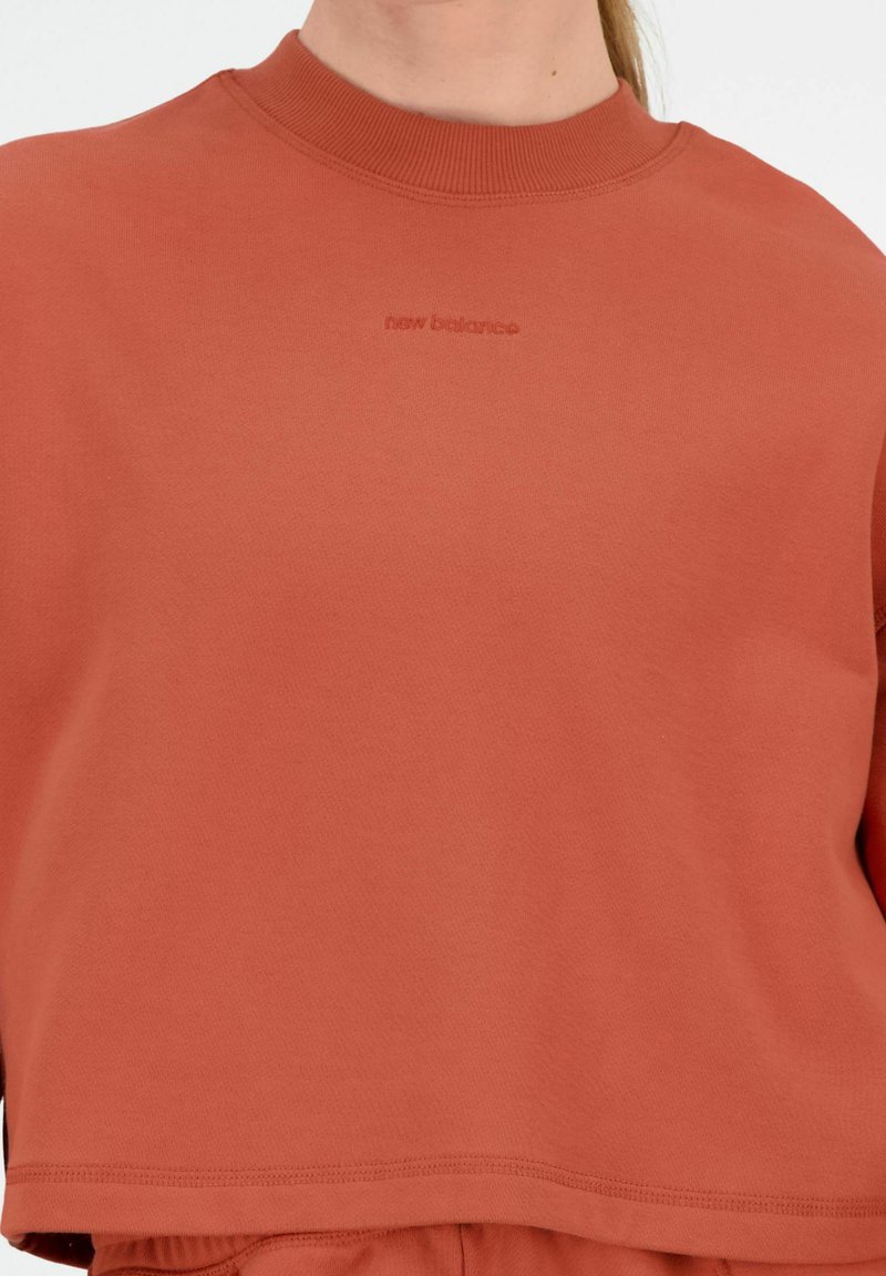 Afgekorte sweatshirt in warme terracotta met een ribbelkraag en verhoogd "new balance" logo. Gladde katoenen mix stof.