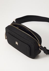 Czarna nylonowa torba na ramię z złotymi zamkami, prostokątny kształt, akcent logo z przodu, regulowany pasek i teksturowany detal wzorniczy.