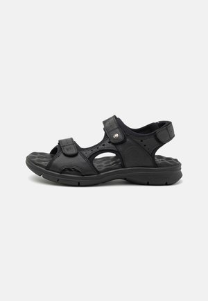 Sandalias de cuero negro con correas ajustables, punta abierta y suela acolchada. Presentan detalles recortados y una marca en el costado.