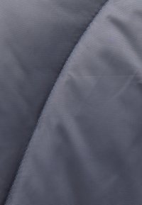 Tejido de nylon gris con una textura suave, que presenta un brillo sutil y un detalle de costura curva a lo largo del borde. Sin patrones ni herrajes visibles.