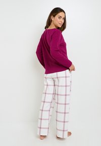 Chemise fuchsia à manches longues avec un col rond, associée à un pantalon blanc avec un motif de grille rouge. Tissu doux, design à coupe décontractée.