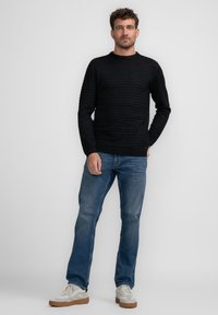 Maglione a righe nere a maglia con collo rotondo, abbinato a jeans in denim blu e sneaker bianche con suola marrone. Un outfit semplice e informale.