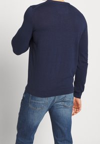 Mörkblå stickad tröja med rund hals, ribbade mudd och nederkant. Bärs med ljusblå denimjeans. Enkel design utan synliga mönster.