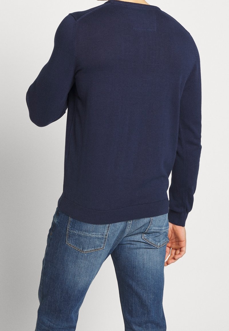 Mörkblå stickad tröja med rund hals, ribbade mudd och nederkant. Bärs med ljusblå denimjeans. Enkel design utan synliga mönster.